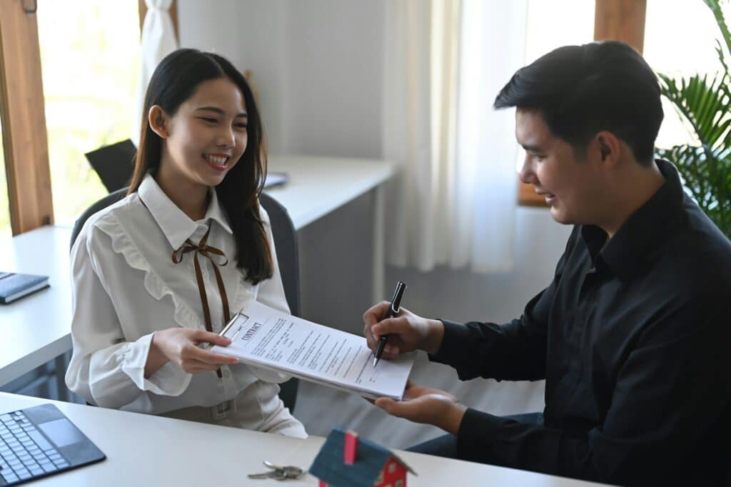 Happy young asian man signing rental contract with real estate broker.