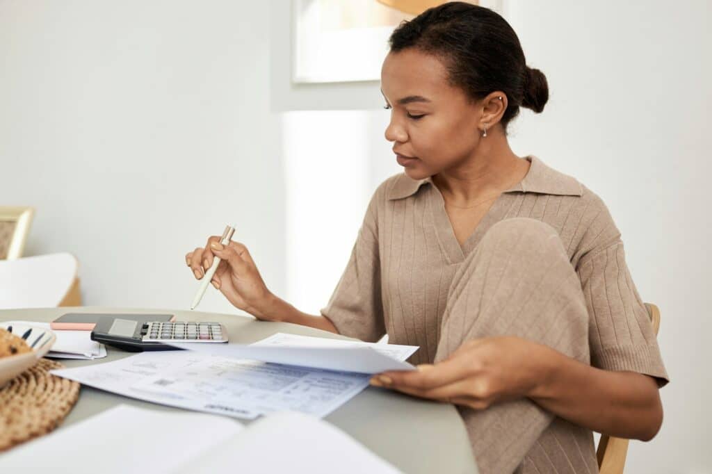 Young Black woman doing taxes at home and using calculator